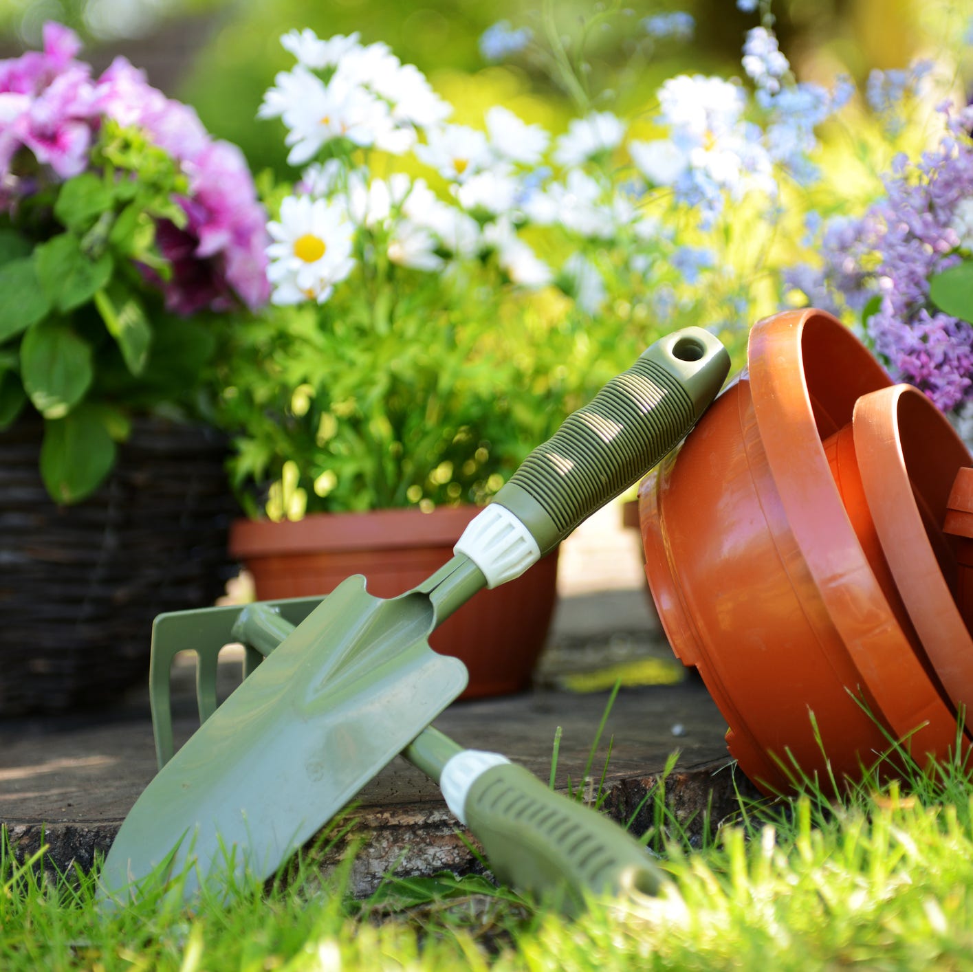 green yard tools next to pots on a green lawn surrounded by potted flowers