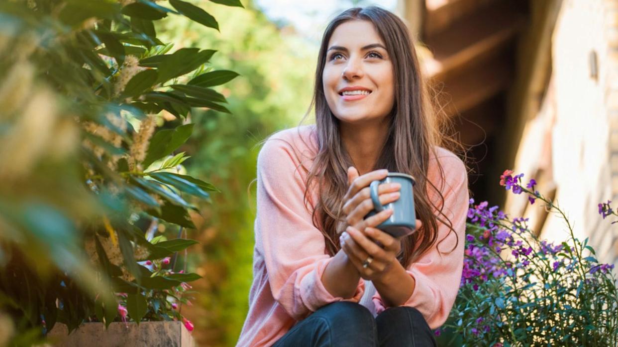 woman enjoying coffee in her garden with purple flowers