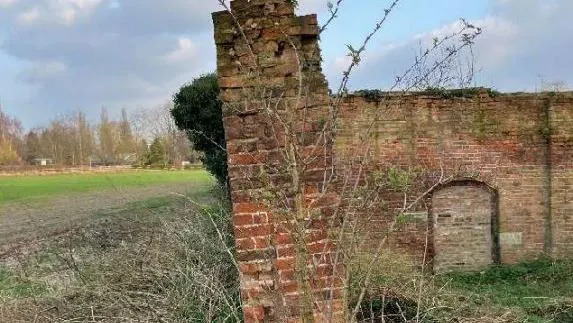 A garden wall of red brick is shown leaning precariously