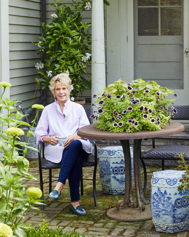 A woman sitting at a table in a garden area with potted plants and flowers. A woman sitting at a table in a garden area with potted plants and flowers.