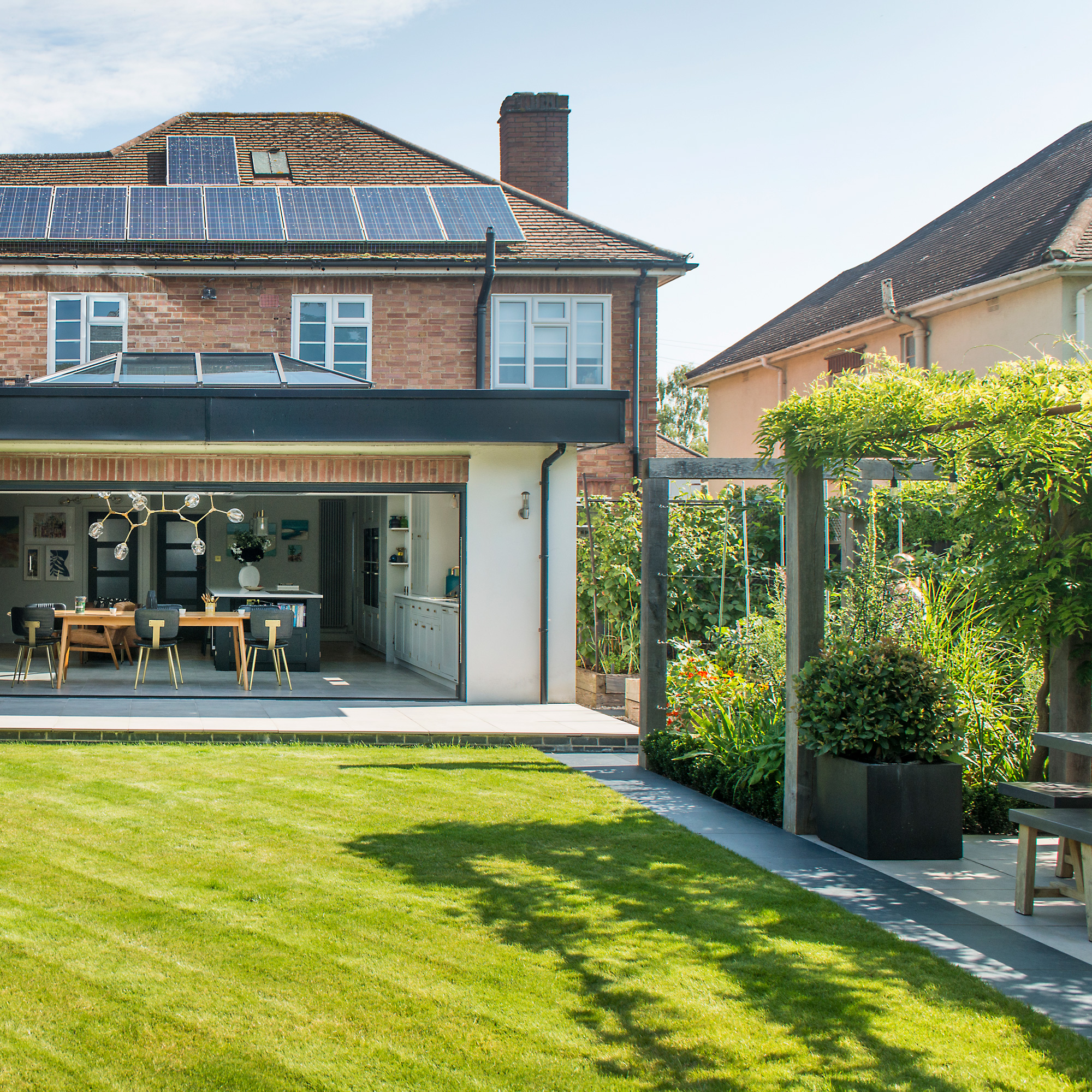 a garden with a large, perfectly kept lawn and and a pergola to one side overa dining area with a large dining table