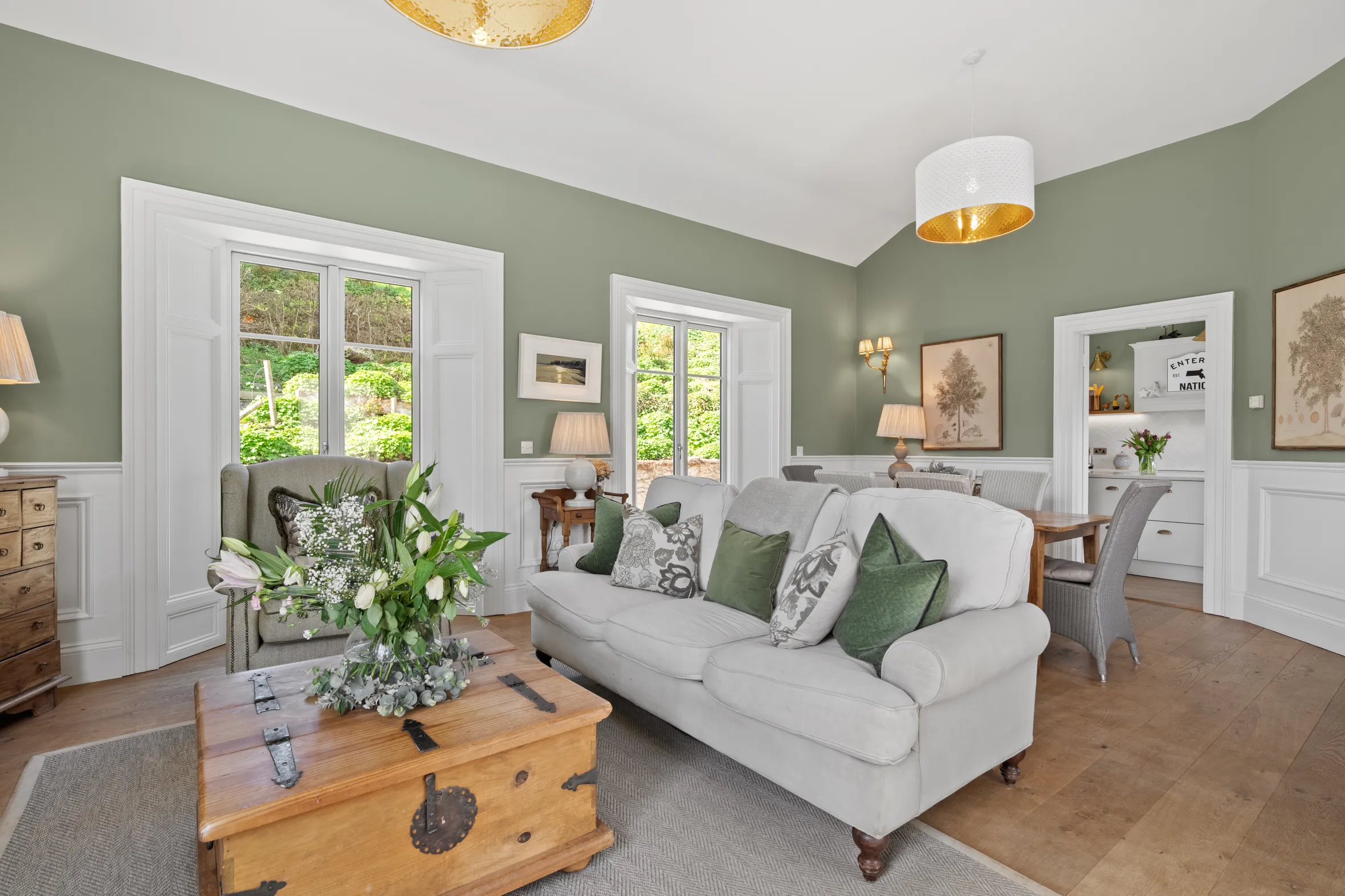 Living room with sage green walls, light gray sofa, and wooden trunk coffee table.