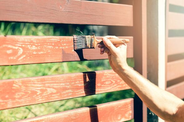 hand with paintbrush painting wooden fence with brown paint hand with paintbrush painting wooden fence with brown paint