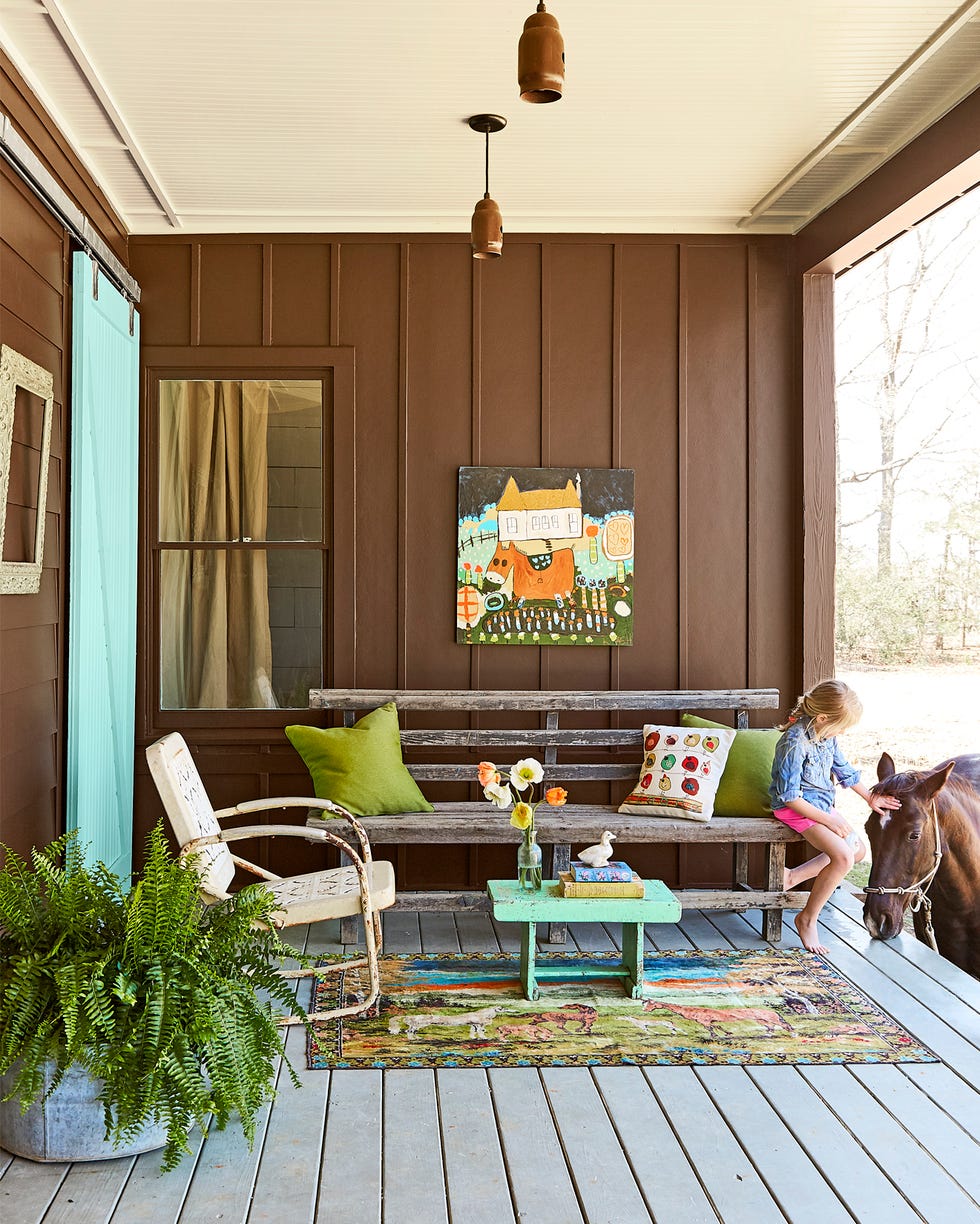 porch with brown walls, rustic bench with green pillows, horse themed decor, and a girl petting a horse