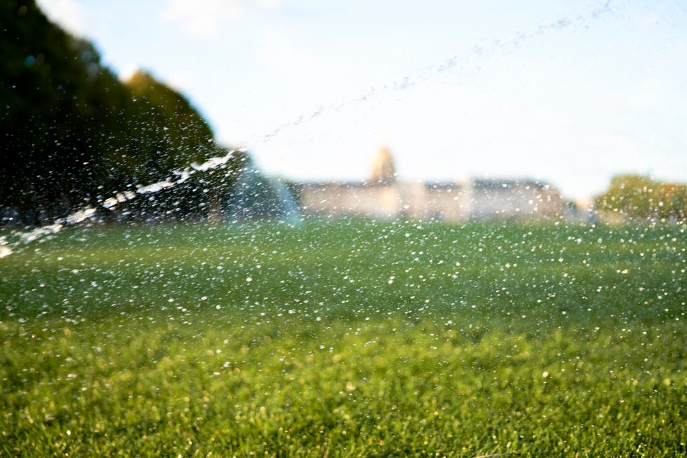 jets of water being thrown with force from automatic watering of grass in a field, side view with a building in the distance jets of water being thrown with force from automatic watering of grass in a field, side view with a building in the distance