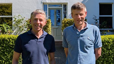 Michael Connolly and Robert Russell wearing blue polo shirts, smiling stood in front of a white house