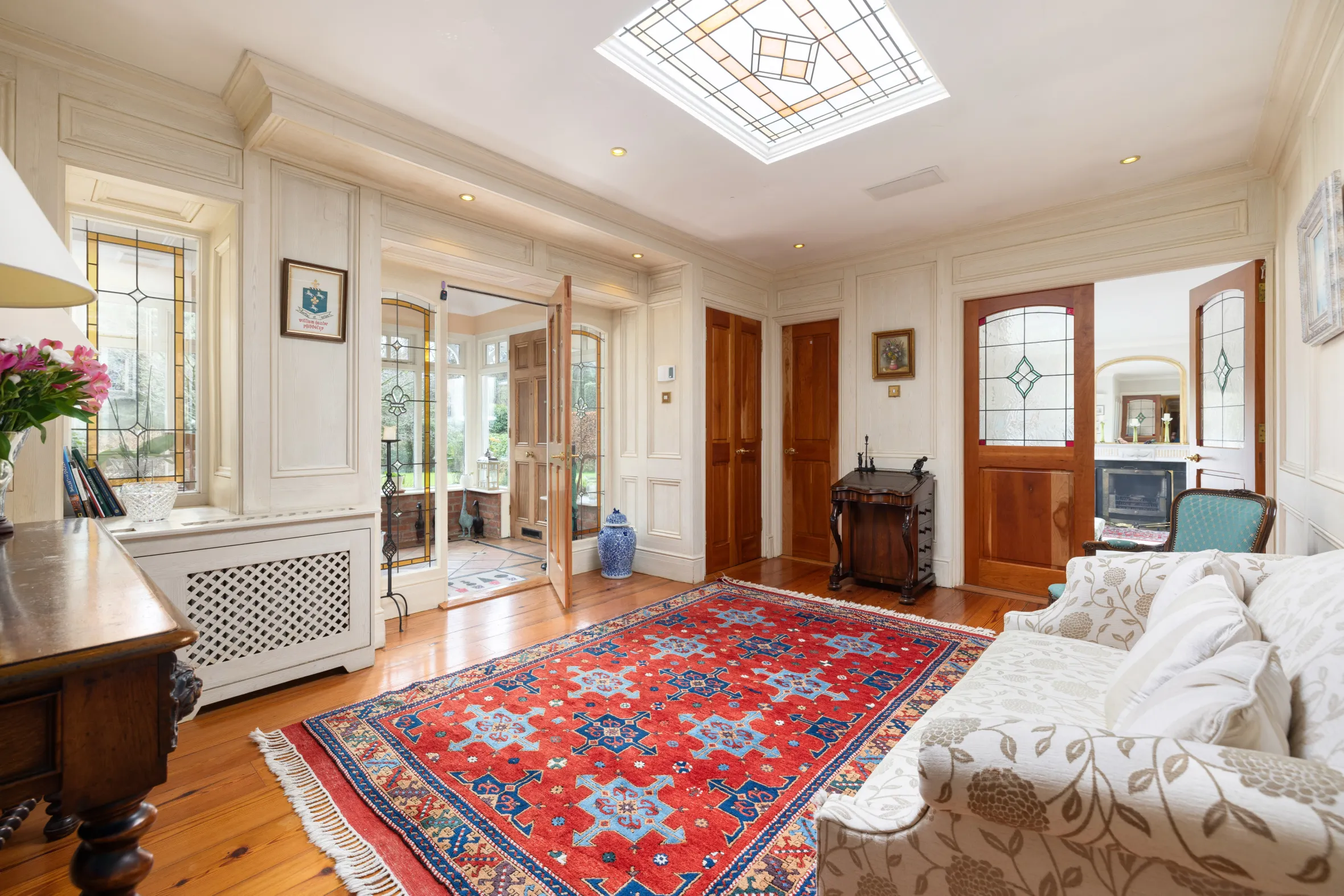 A living room featuring a patterned red and blue area rug, cream-colored sofa, and a skylight.