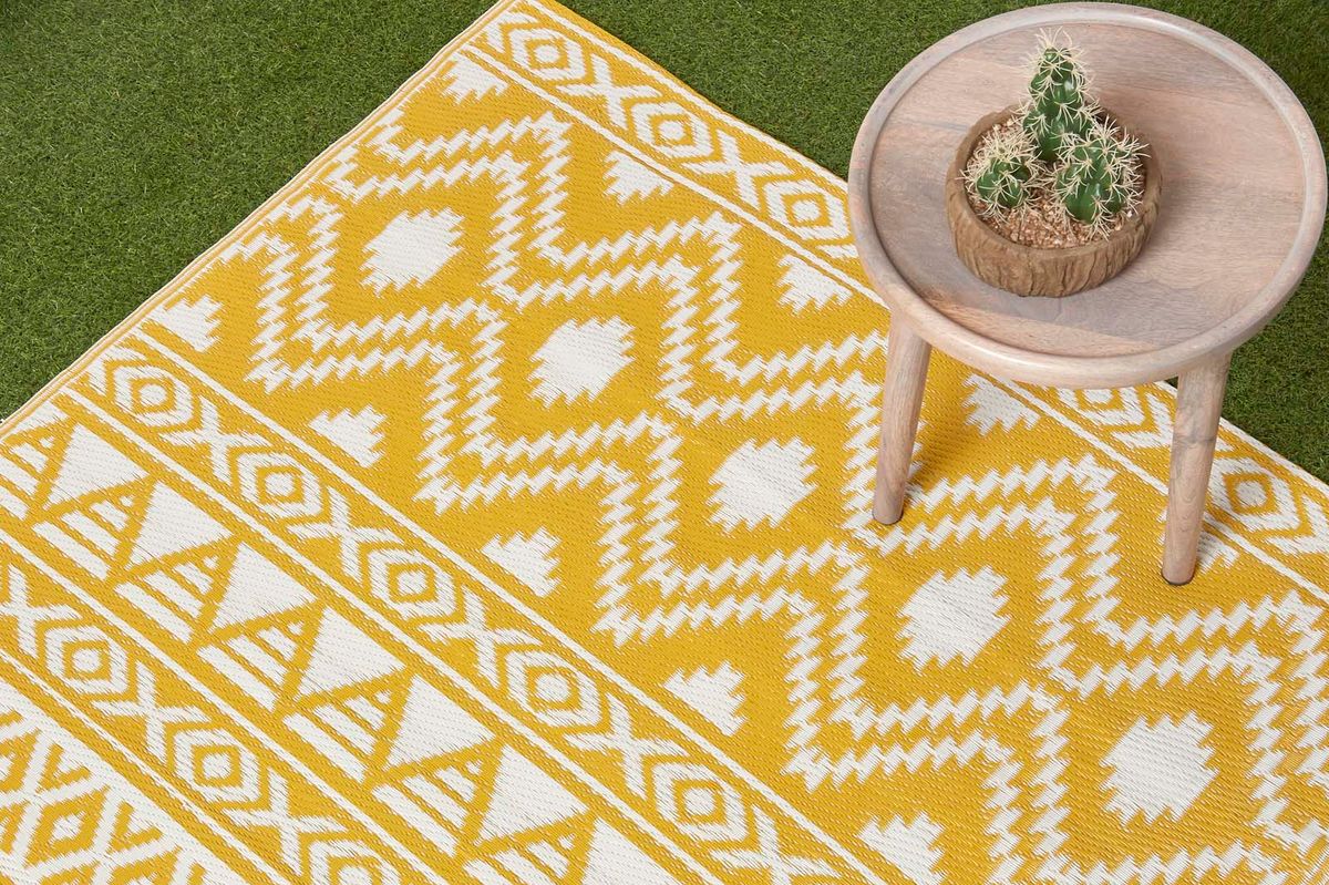 The yellow Aztec outdoor rug on grass with a small table on it