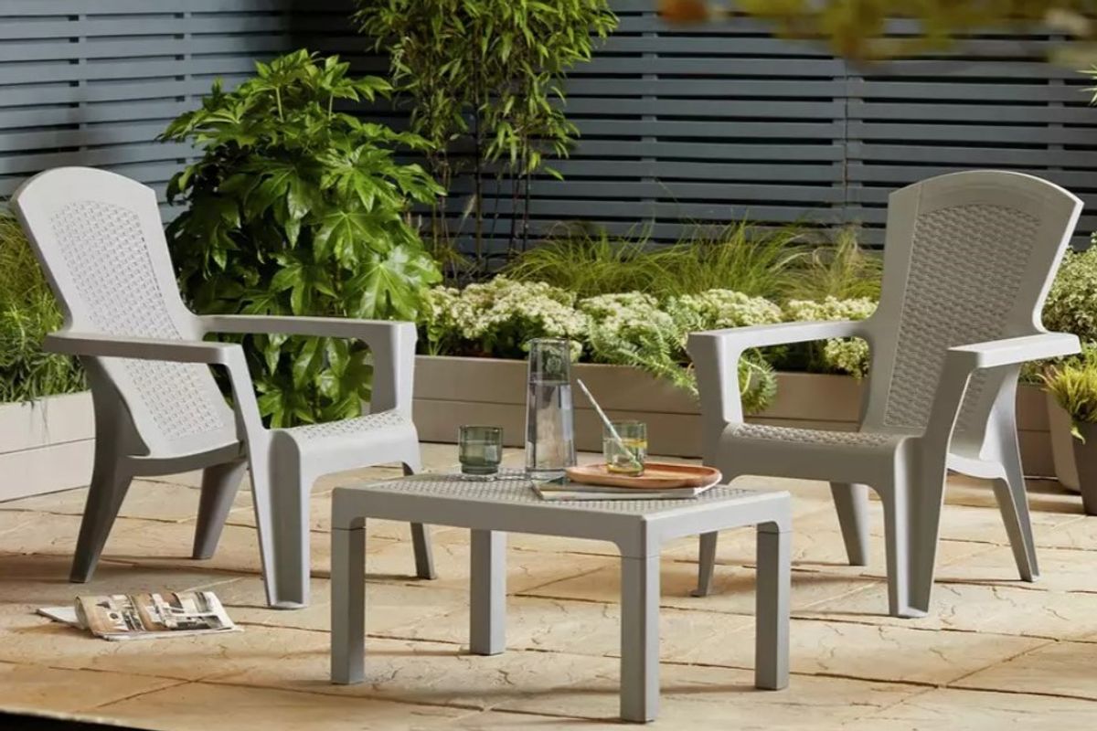 A grey plastic bistro set with two chairs and a small table set up on a flagstone patio area of a garden.