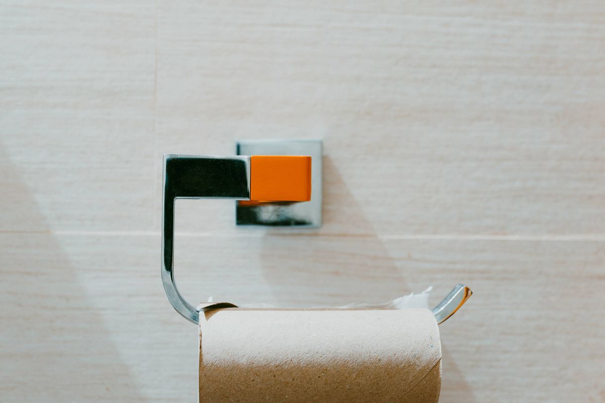 Last piece of toilet paper in a roll on a beige wall. Empty toilet paper roll. Minimalist composition. Concept of problems and crisis.