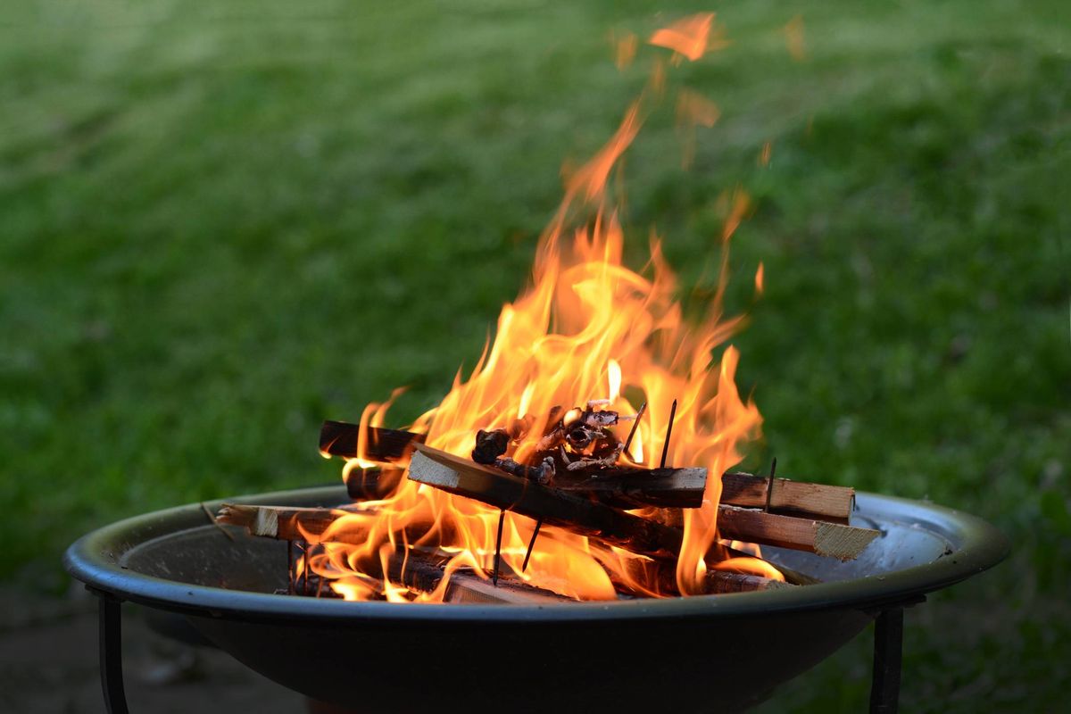 A circular outdoor fire pit with burning wood and flames, situated on a grassy background.