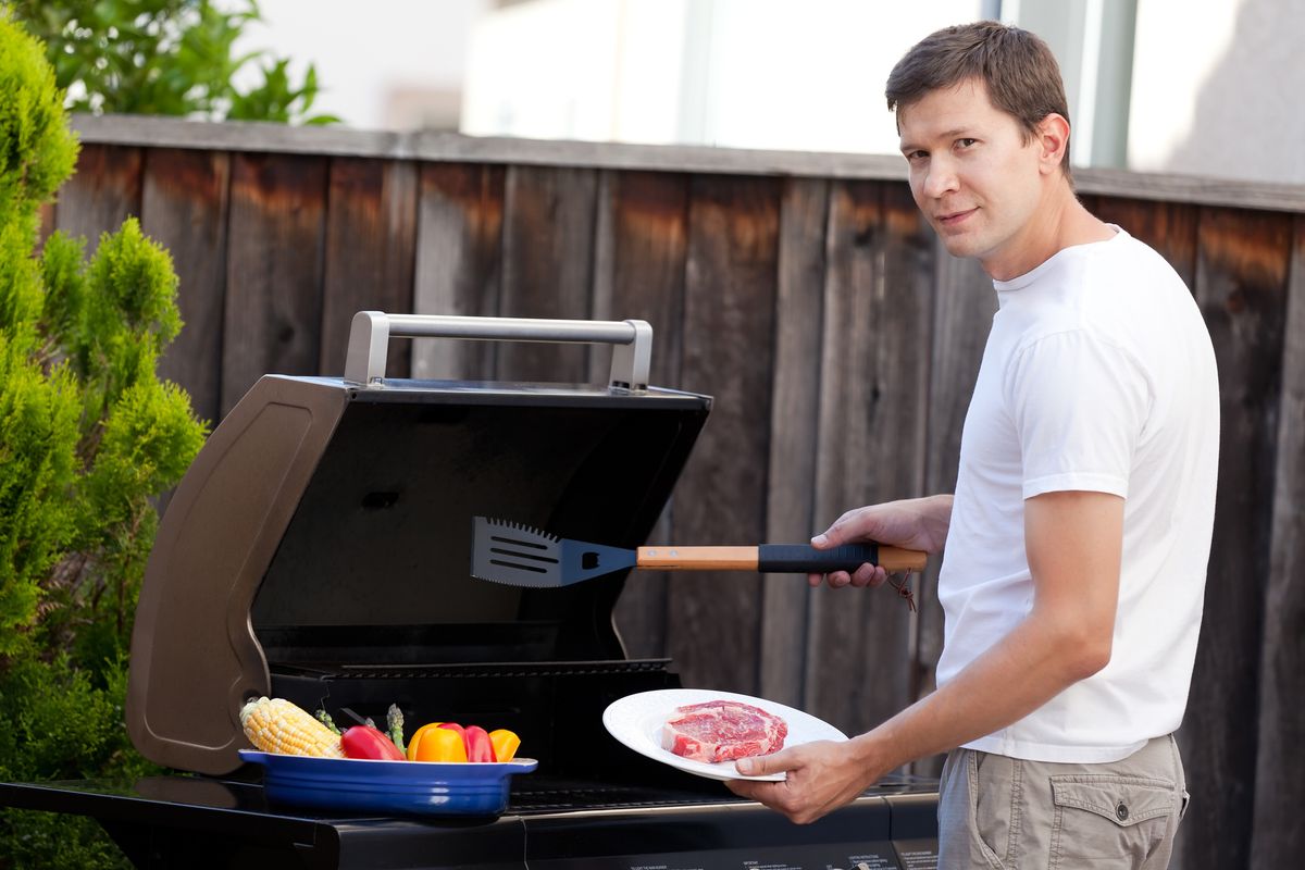 young handsome man ready for grilling meat and vegetables at his house backyard