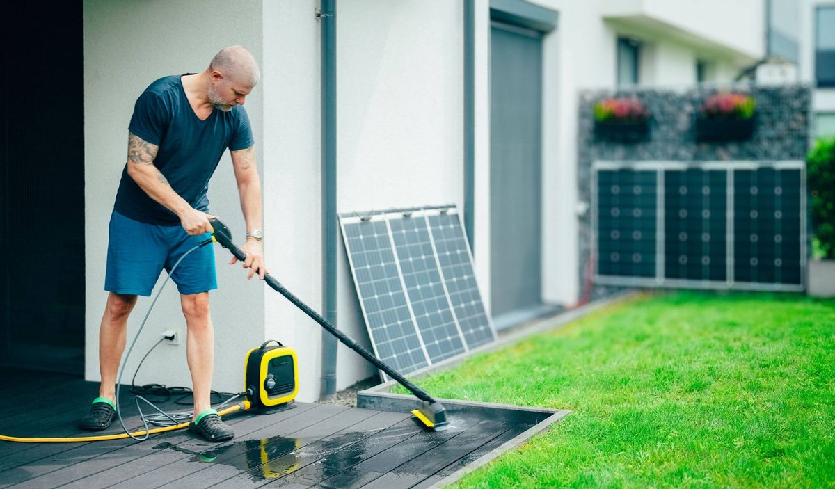 Man cleaning terrace with pressure washer at home