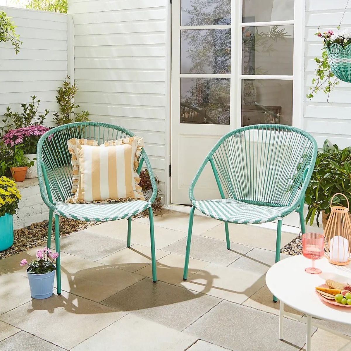 A set of two green and white rattan chairs on a flagstone patio.