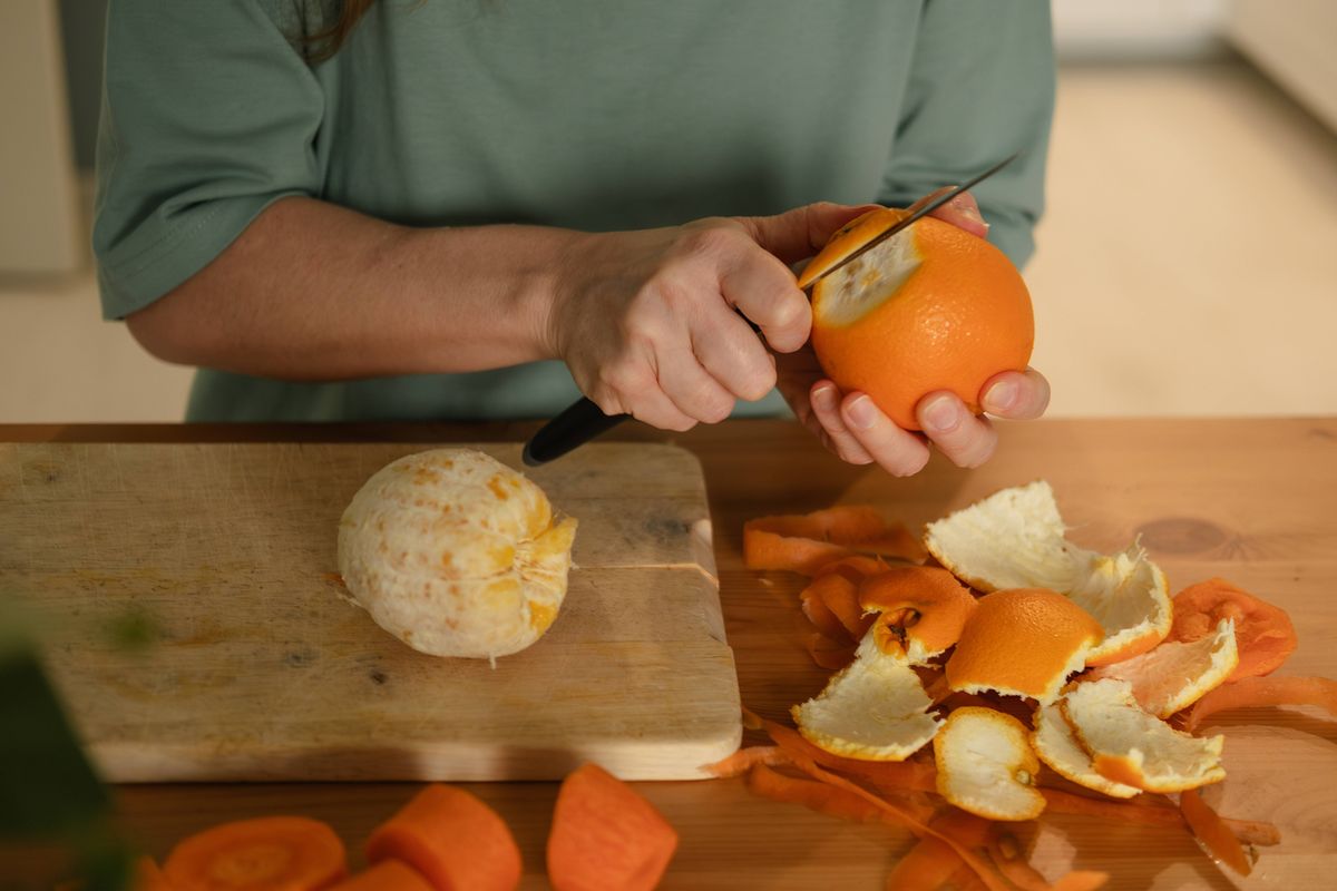 woman peeling an orange at the kitchen table at home. Hands close up