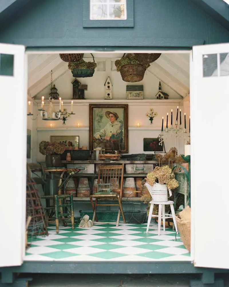 Cozy garden shed interior with green and white checkered floor, vintage furniture, potted plants, and decorative items.