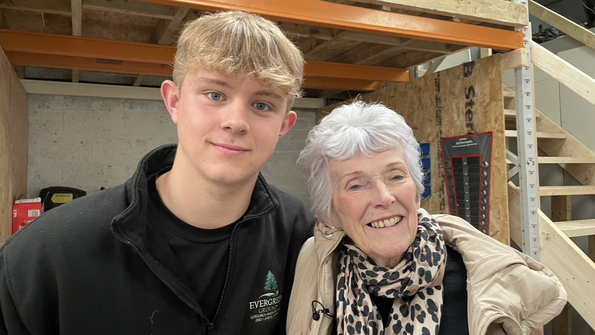 Jack Roberts is pictured standing with his arm around his grandmother, Wendy Richardson, who smiles into the camera. Wendy has short, styled white hair and is wearing a leopard-print scarf, black t-shirt and beige coat.