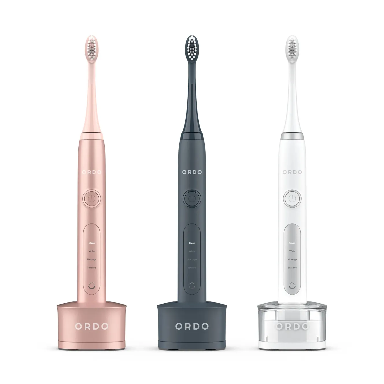 Three Ordo sonic electric toothbrushes in rose gold, charcoal grey, and white, each on a charging base.
