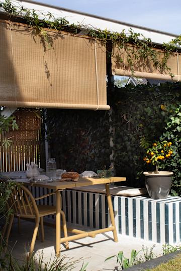 a garden with a dining area with a wood table and striped tile bench surrounded by foliage