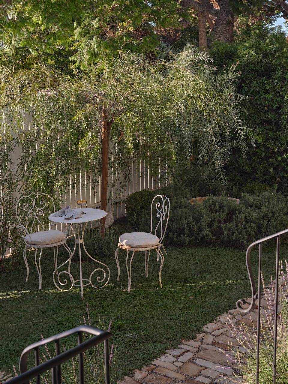 Small outdoor seating area with a table and two chairs surrounded by greenery.