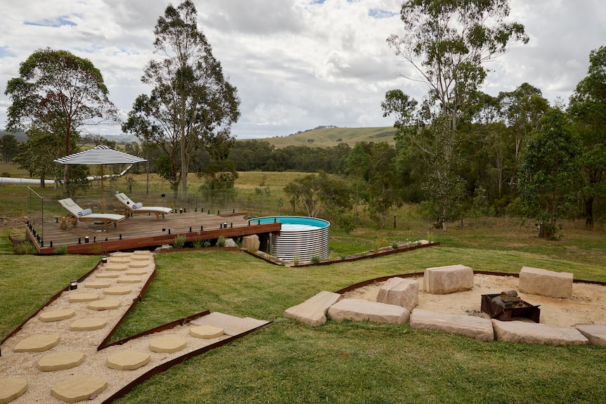 A back yard with a firepit and a deck leading to a plunge pool.