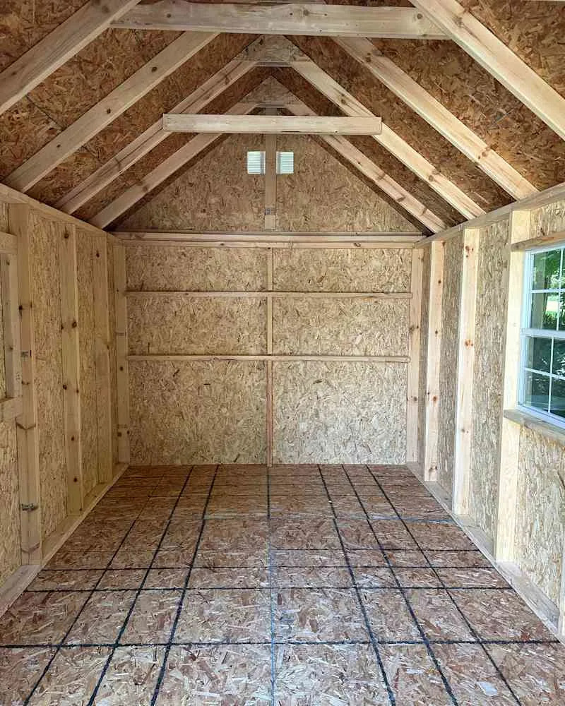 Interior of a wooden shed with exposed OSB walls, a peaked roof, and a grid-patterned floor.
