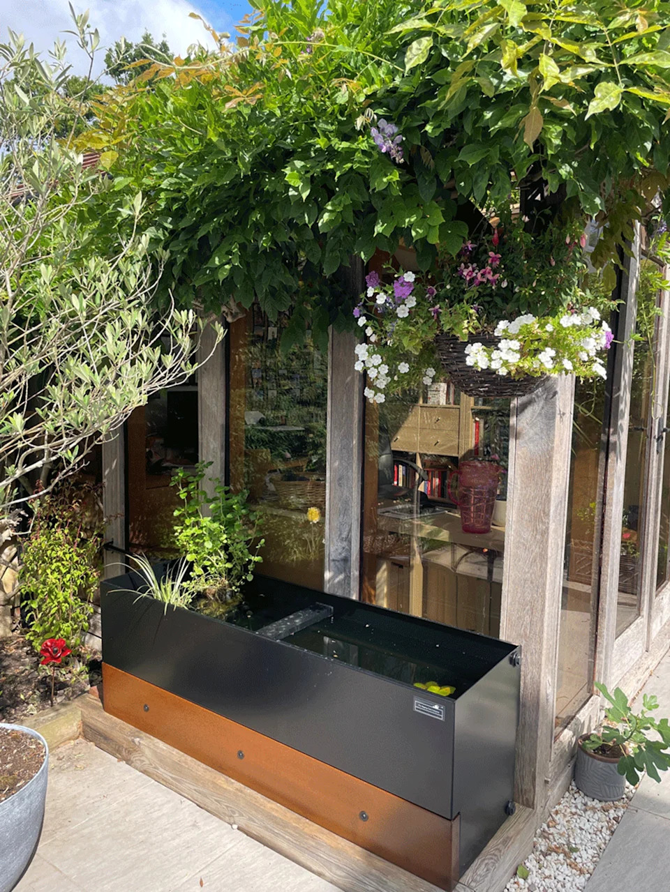 a dipping tank in a garden next to an outdoor structure surrounded by plants