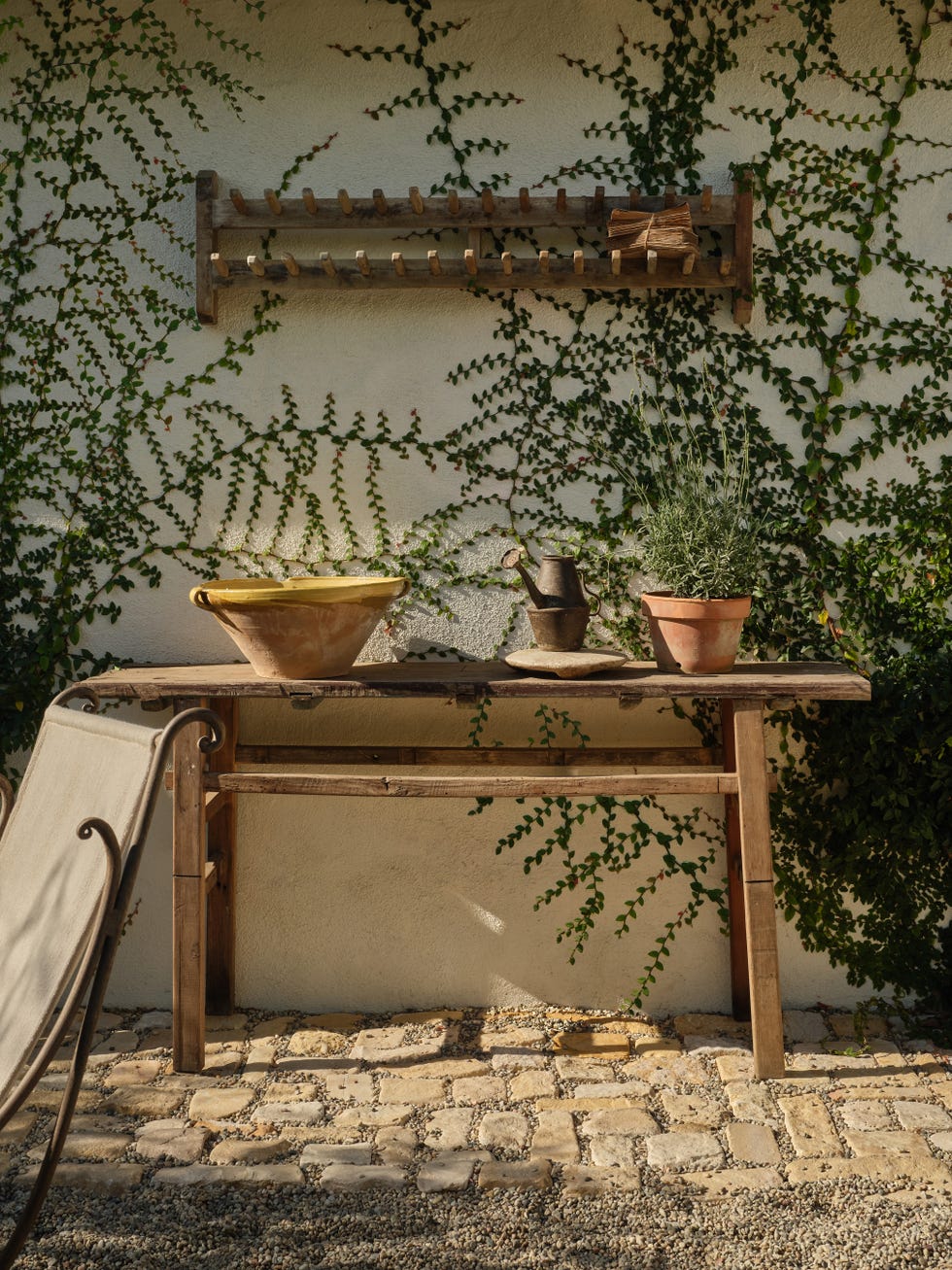 Garden table with pots and greenery against a wall.