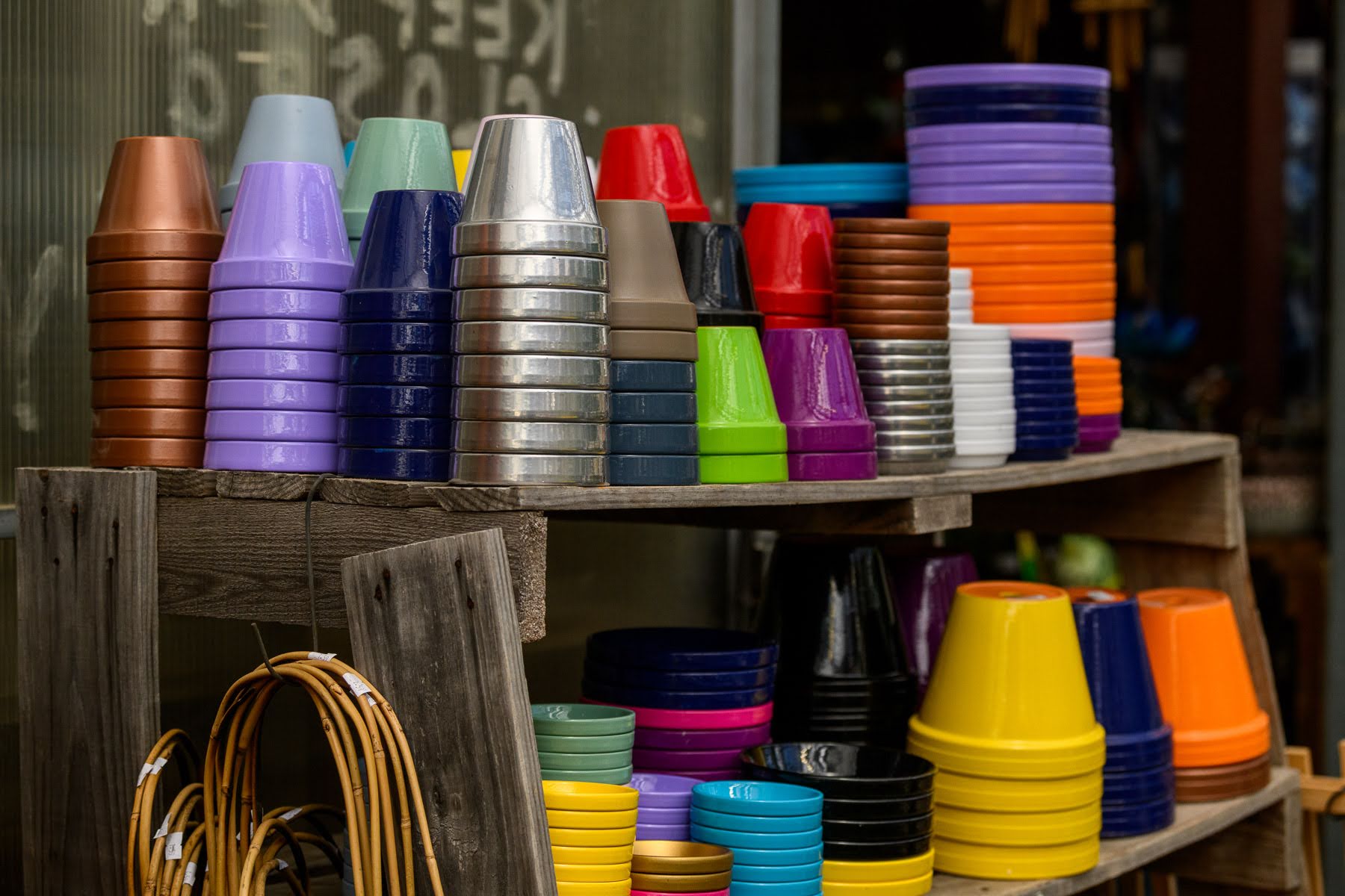 Stacks of colorful plastic plant pots in various sizes are arranged on wooden shelves outdoors.