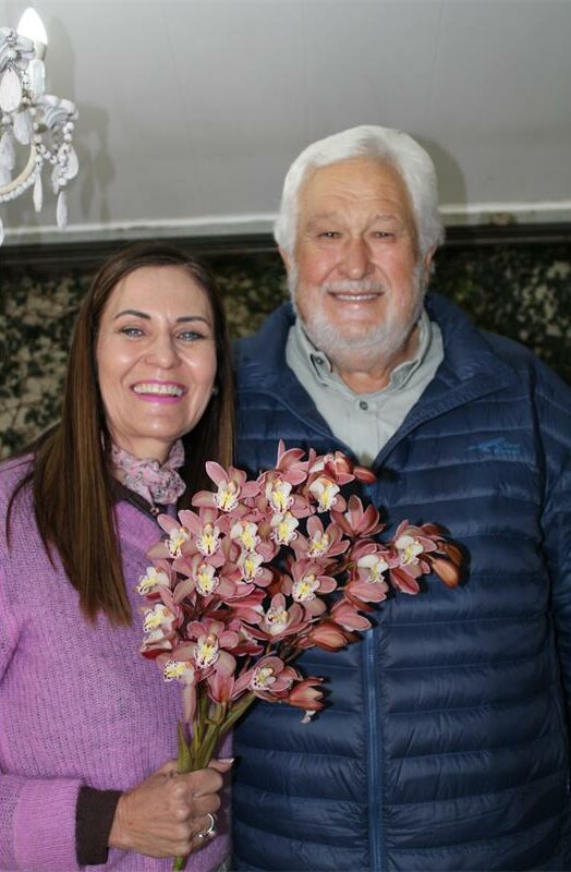 Woman stands next to a grey haired man, holding a bunch of flowers