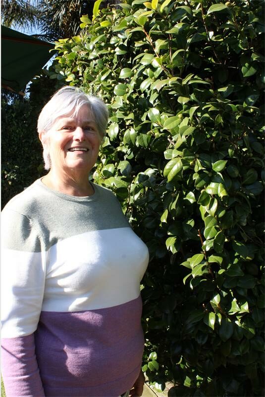Elderly woman standing next to a shrub