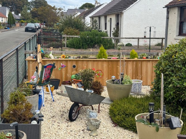 The wooden planter which has sparked a row between neighbours. // A retired widow became embroiled in a bizarre neighbour planning row - after being accused of 'spending hours' attending to her new planter. Jane Higgins, 74, had the planter installed in the front garden of her semi detached home and spends her time tending to the plants, flowers and ornaments within it. But her family were shocked when they were told they needed to apply for retrospective planning permission for structure - as a neighbour had issued a complaint. Among the concerns raised by the one objector were that it overshadows their privacy "as the neighbour spends hours attending to their plants." Photo released 17/05/2026