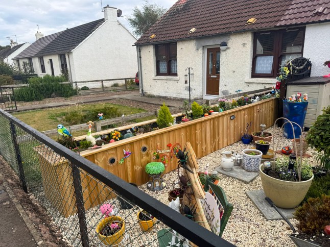 The wooden planter which has sparked a row between neighbours. // A retired widow became embroiled in a bizarre neighbour planning row - after being accused of 'spending hours' attending to her new planter. Jane Higgins, 74, had the planter installed in the front garden of her semi detached home and spends her time tending to the plants, flowers and ornaments within it. But her family were shocked when they were told they needed to apply for retrospective planning permission for structure - as a neighbour had issued a complaint. Among the concerns raised by the one objector were that it overshadows their privacy "as the neighbour spends hours attending to their plants." Photo released 17/05/2026