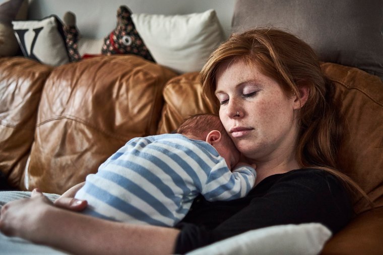 A mother and new born baby taking a nap together on the sofa in a quiet but tender moment.