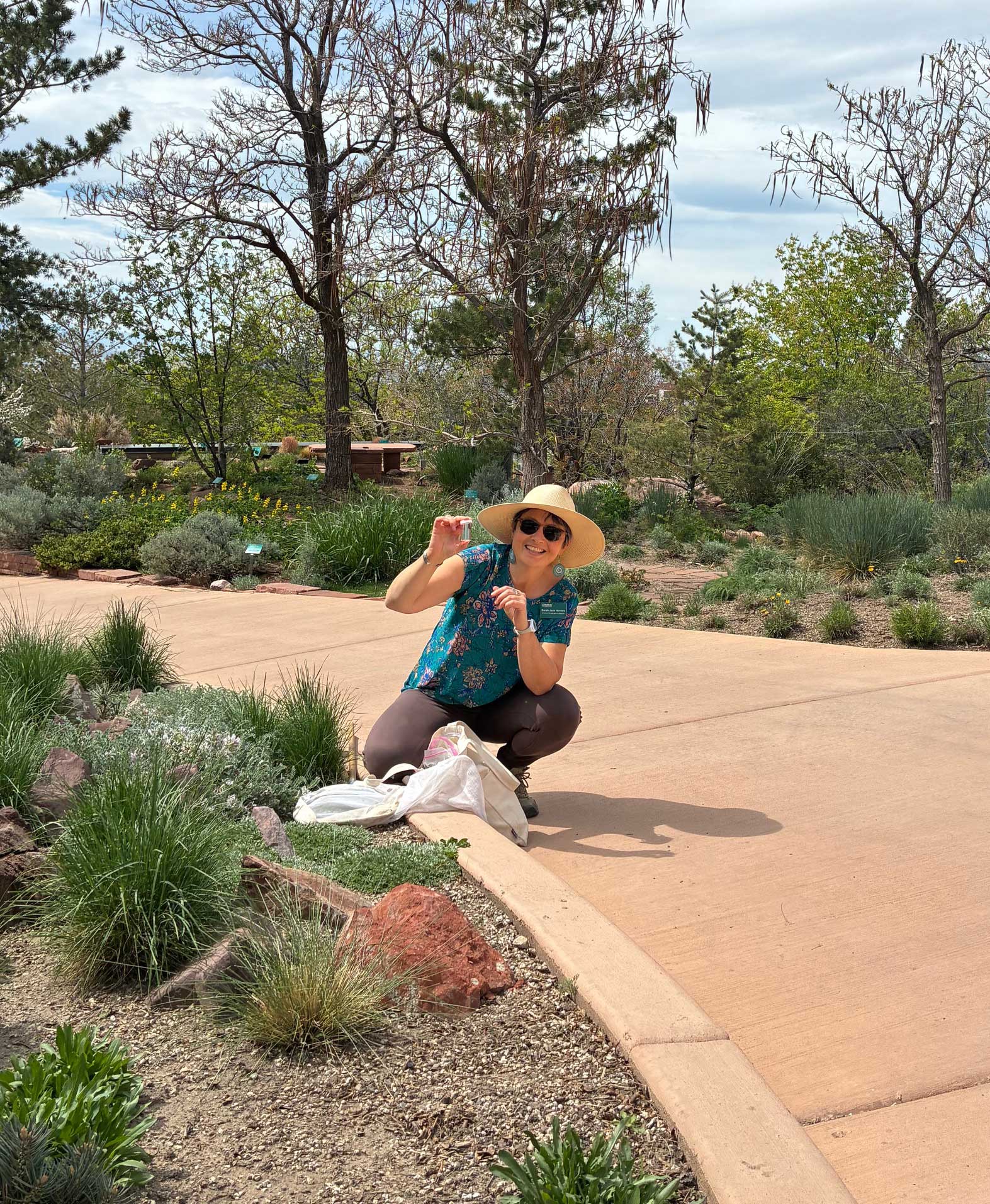 A woman crouches down in a garden holding up a small bee with a net in front of her.
