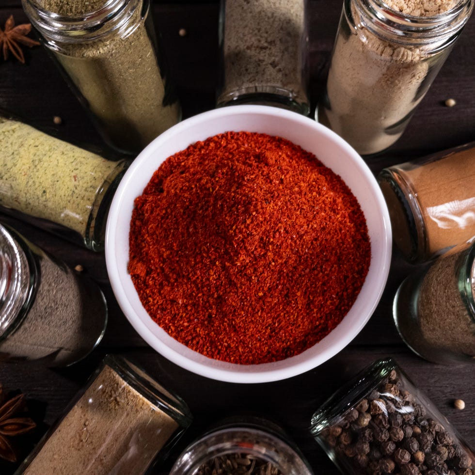 A vibrant arrangement of various spices and seasonings in glass jars a vibrant arrangement of various spices and seasonings in glass jars, with a focus on red pepper powder in a white bowl, ideal for culinary themes and food photography