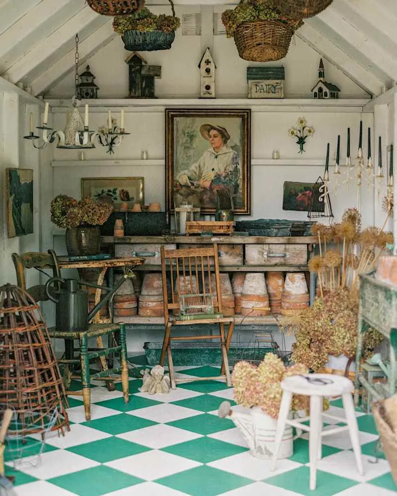 Cozy garden shed with vintage decor, green and white checkered floor, wooden furniture, and potted plants.