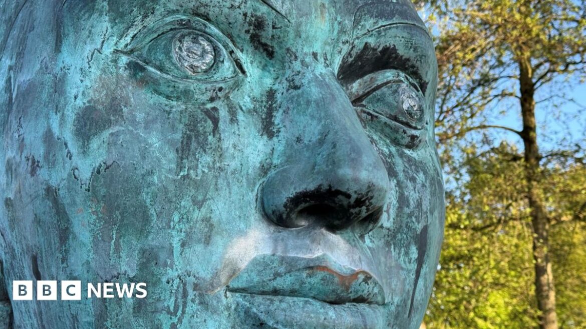 Searching for the artistic legacy of Stoke-on-Trent’s 1986 National Garden Festival A close-up of a green-coloured sculpture of a face is seen with trees in the background. There are scratches on the sculpture's eyes.