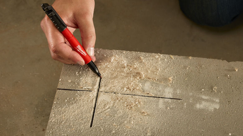 A Milwaukee marker being used to draw an X on concrete.