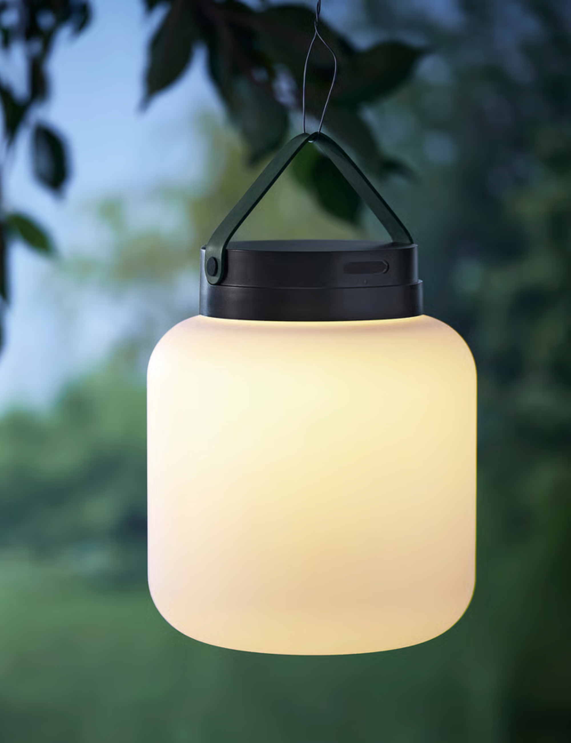 IKEA L&Auml;NSPORT lamp softly aglow, hanging from a leafy tree branch.