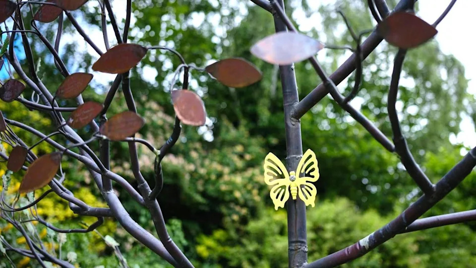 A close up of a metal tree sculpture with a metal yellow butterfly and copper leaves