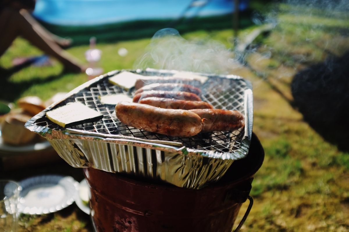 A person cooking sausages on a disposable BBQ