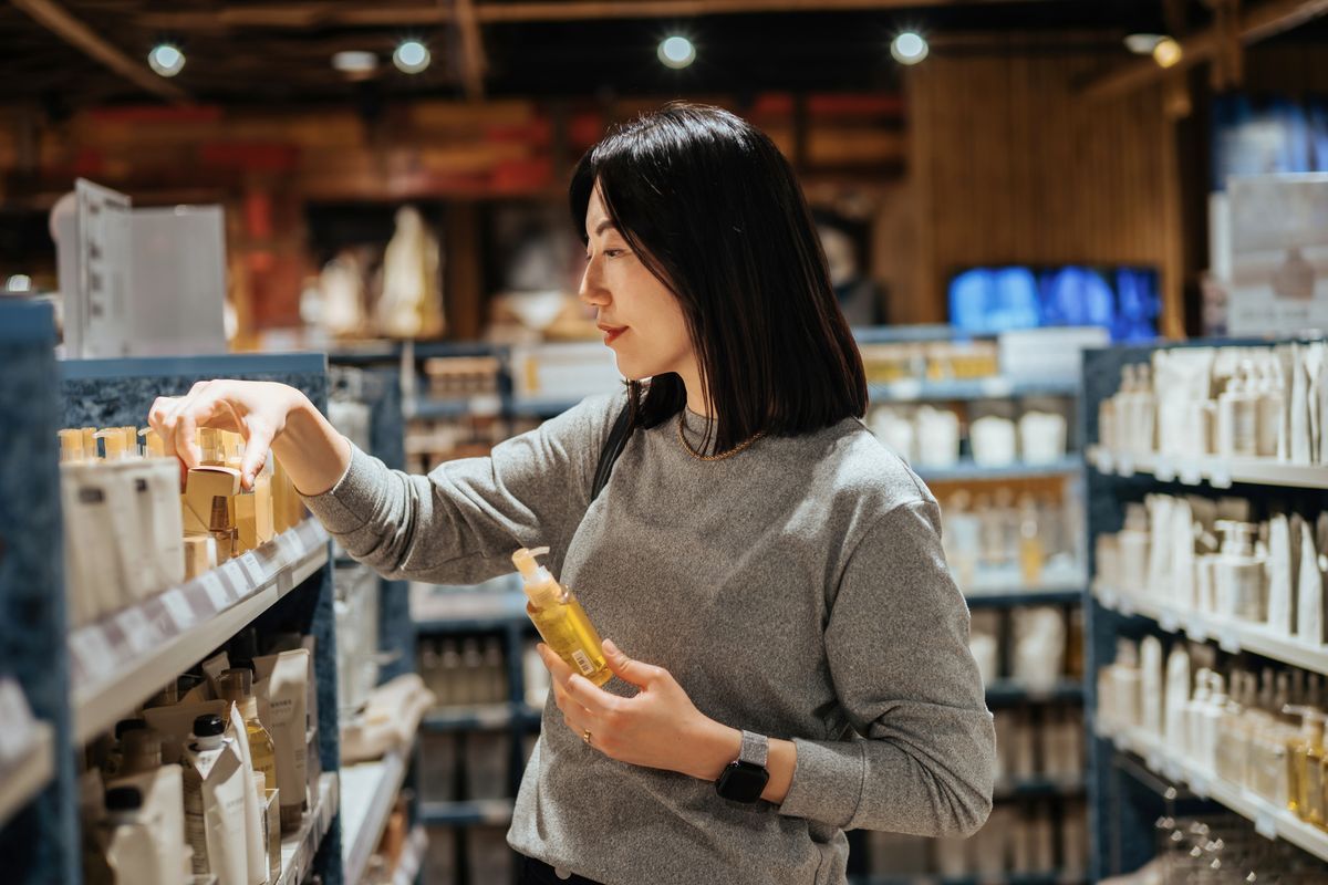 Young Asian woman shopping for natural beauty products in organic health and beauty store. Comparing and looking at the ingredients of the skincare package. Cosmetics and beauty products. Health and wellness concept. Sustainable lifestyle