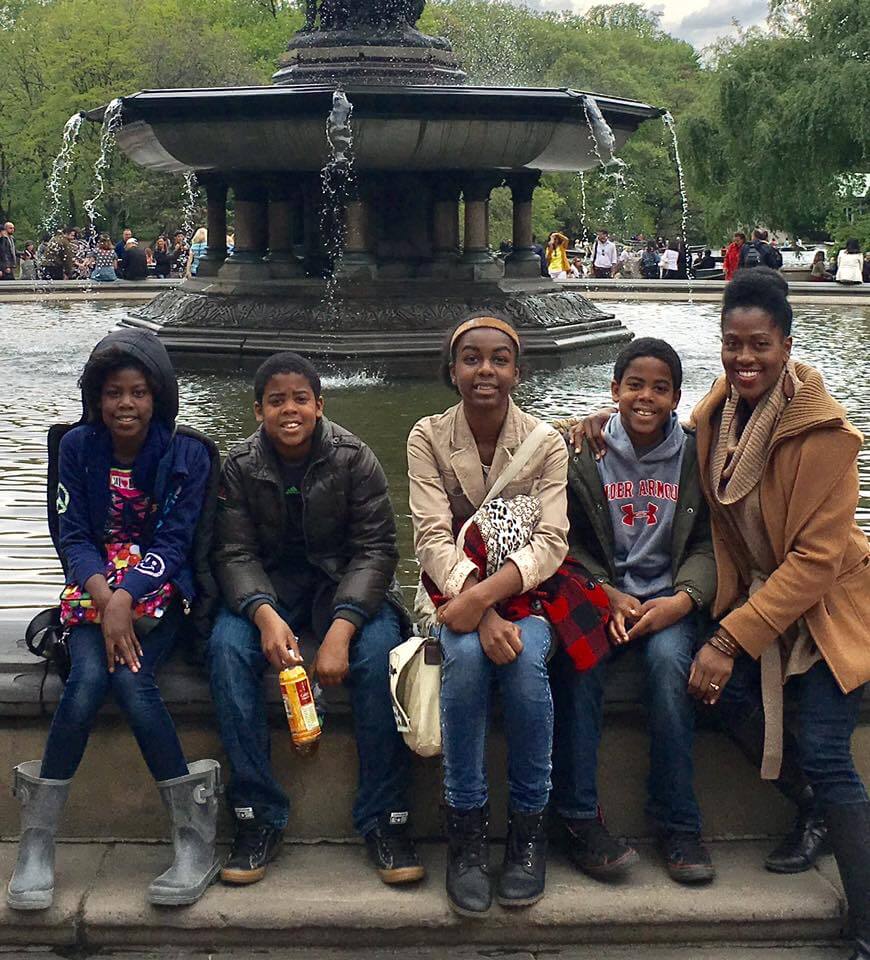 She Shapes Creativity & Community at Carpenter Art Garden - 5 Ayanna Murray and four others sit on the edge of a fountain in a park. Trees and other people can be seen in the background.
