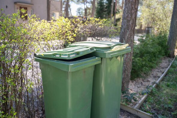 Two garbage bins stand by fence of house Two garbage bins stand by fence of house