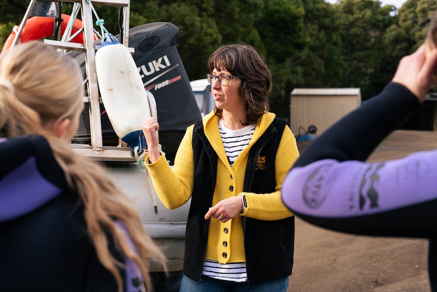 Pauline Nutten a dive instructor with cropped brown hair in a yellow woollen jumper and black vest on land.