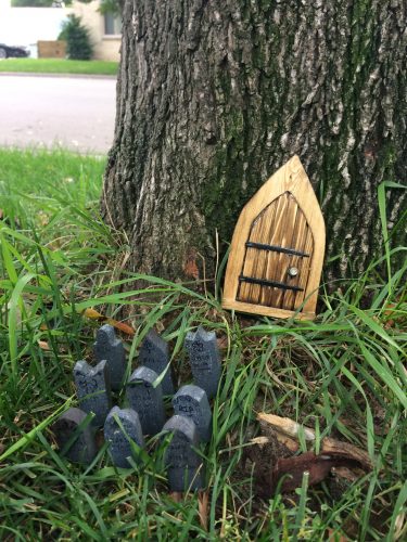 Tiny church door by tree trunk, and nine tiny gravestones with fairy writing