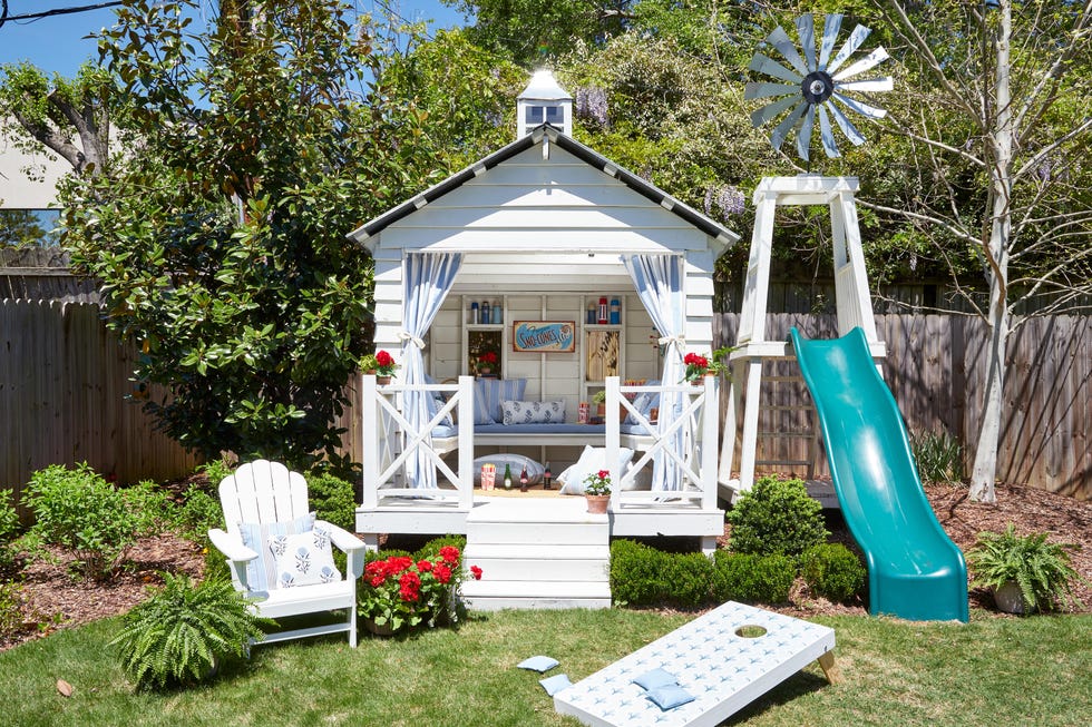Charming backyard playhouse with a slide, lawn games, and decorative flowers surrounded by greenery.