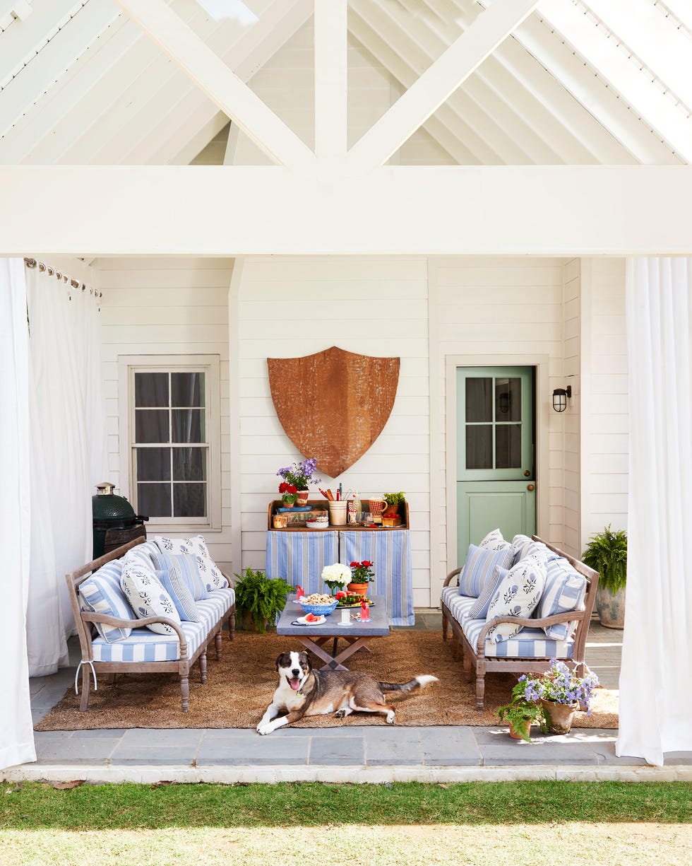 Cozy outdoor living space with seating, a table of snacks, potted plants, and a dog resting on the floor.
