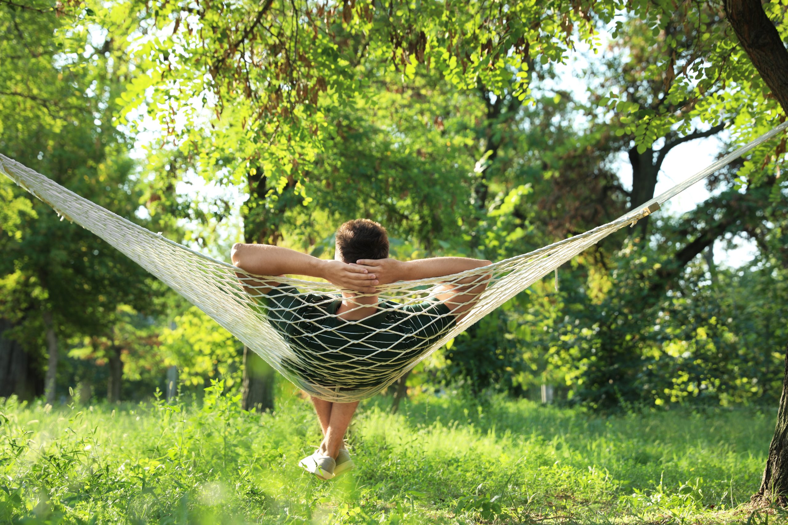 young man resting in comfortable hammock, backyard